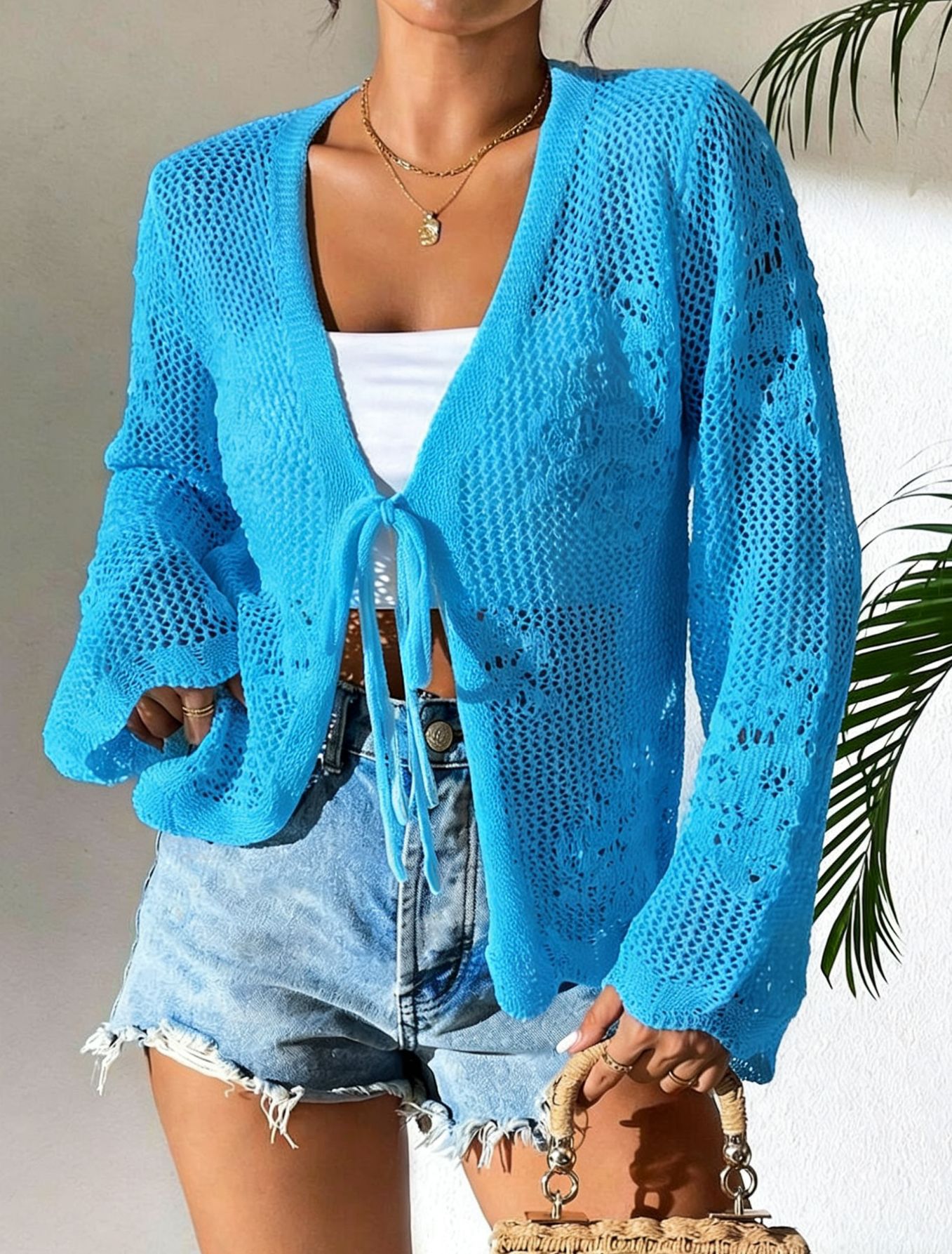 Close-up detail of women's hollow-out lace-up knit cardigan – open knit texture and lace-up front in White