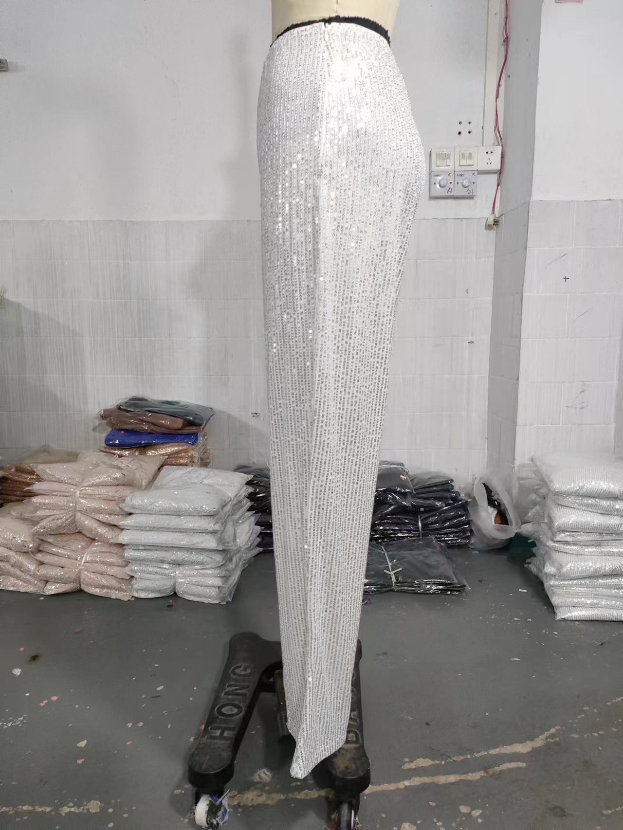 Actual white sequin trousers on a mannequin, showing the embellished fabric, fitted upper leg and flared hem in side view