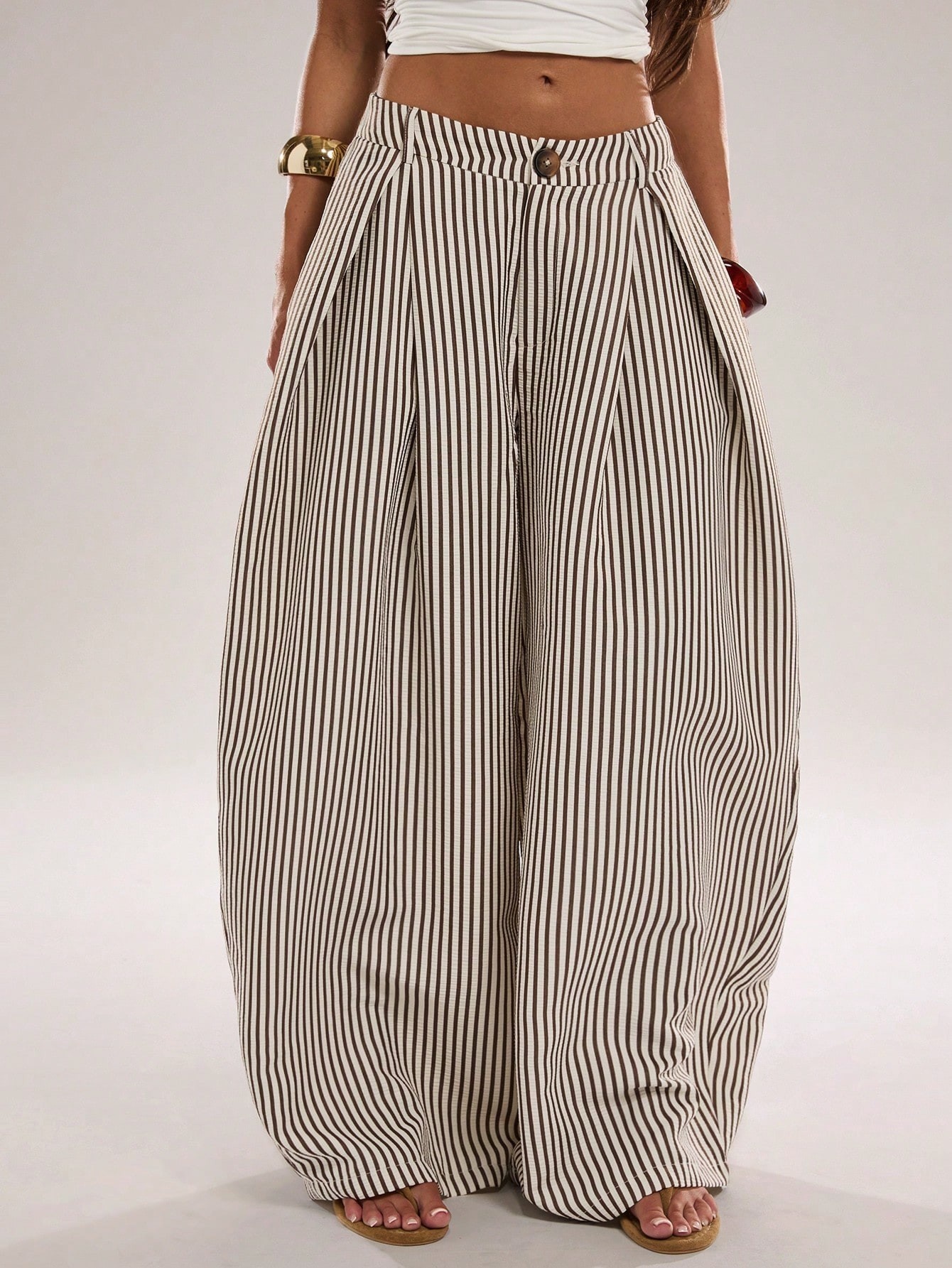 Close view of striped wide-leg trousers showing the front button, belt loops and deep pleats