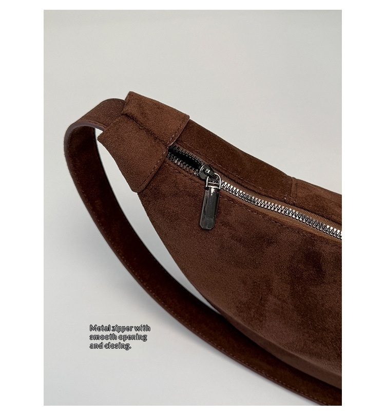 Close-up of the brown crescent bag showing the suede-look surface, stitched strap attachment and top zip