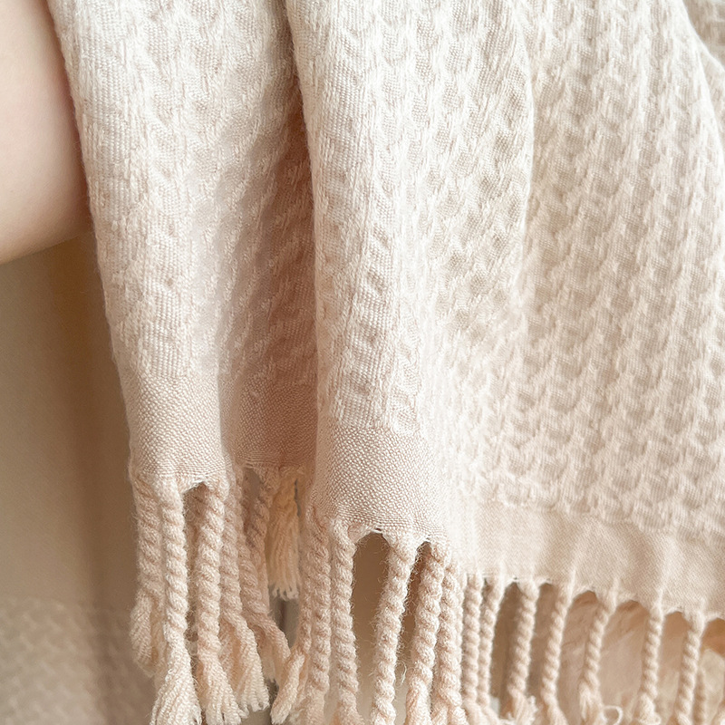 Close-up of the beige shawl showing its raised jacquard texture, smooth border and twisted tassel fringe